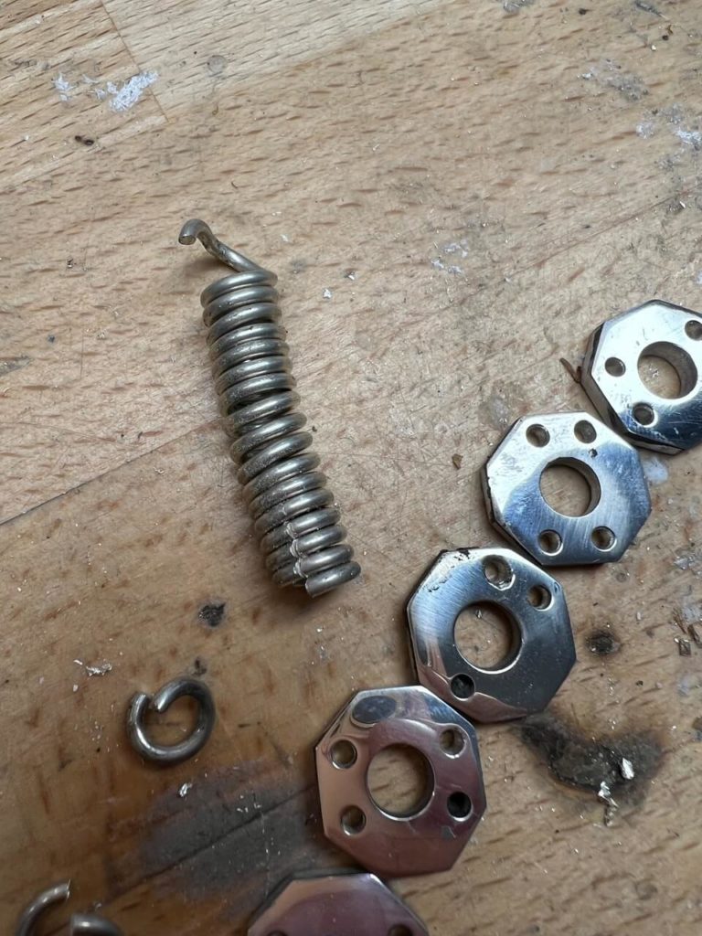Metallteile für eine Schmuckreparatur bei Goldwerk Berlin-Lankwitz: eine Spiralfeder und mehrere sechseckige Metallelemente auf einer Werkbank.