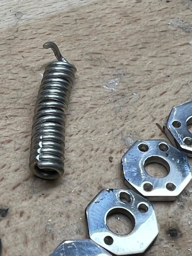 Metallteile für eine Schmuckreparatur bei Goldwerk Berlin-Lankwitz: eine Spiralfeder und mehrere sechseckige Metallelemente auf einer Werkbank.
