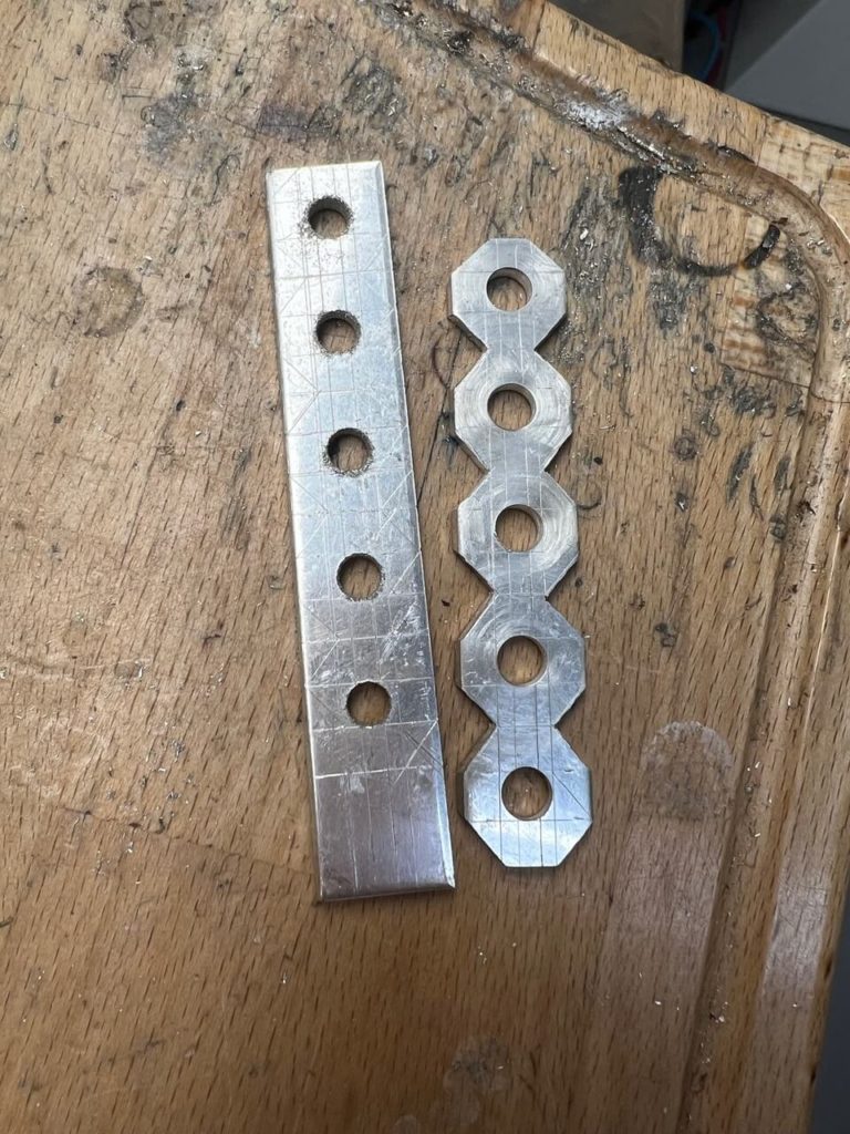 Zwei Metallstreifen mit Bohrungen auf einer Werkbank in unserer Goldschmiede in Berlin-Lankwitz.