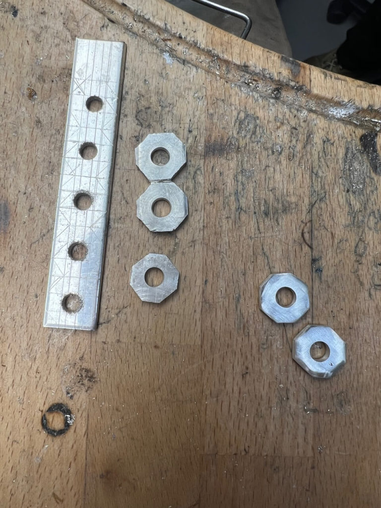 Metallstreifen mit Bohrungen und mehrere achteckige Metallelemente auf einer hölzernen Werkbank in unserer Berliner Goldschmiedewerkstatt.