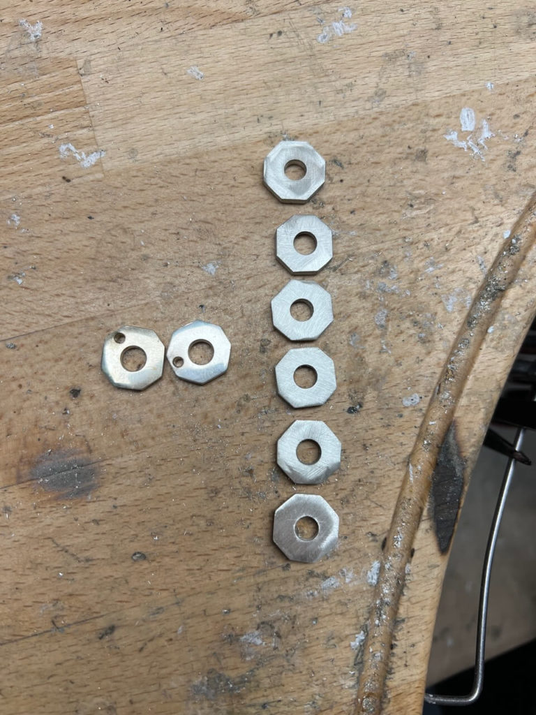 Mehrere achteckige Metallplättchen aus Silber auf einer hölzernen Werkbank in der Goldschmiedewerkstatt von Goldwerk in Berlin-Lankwitz bei der Arbeit.