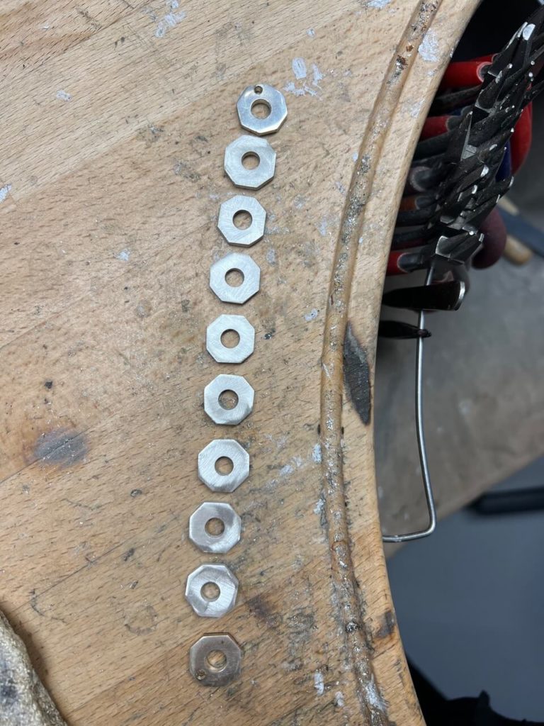 Mehrere achteckige Metallelemente auf einer hölzernen Werkbank in unserer Berliner Goldschmiede, bereit für die individuelle Schmuckanfertigung.