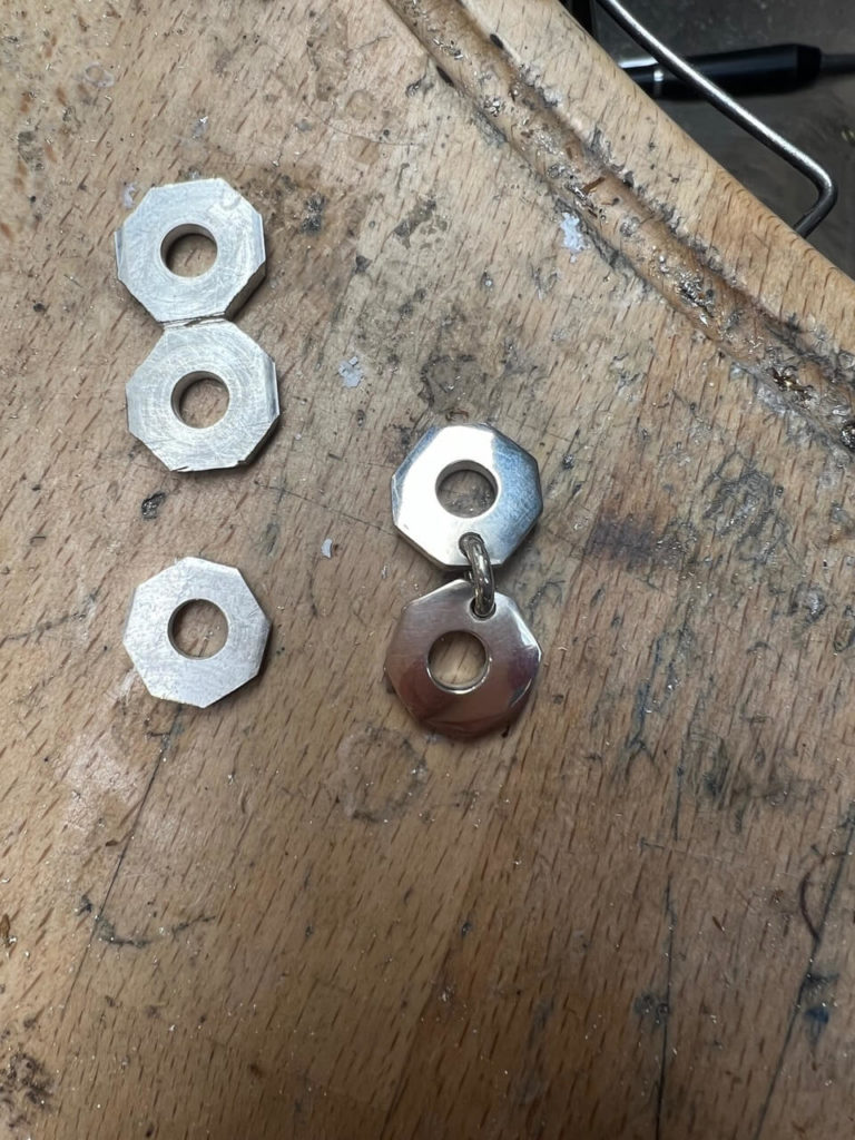 Handgefertigte Schmuckelemente in Sechskantform aus Silber auf einer hölzernen Werkbank in unserer Berliner Goldschmiede-Werkstatt.