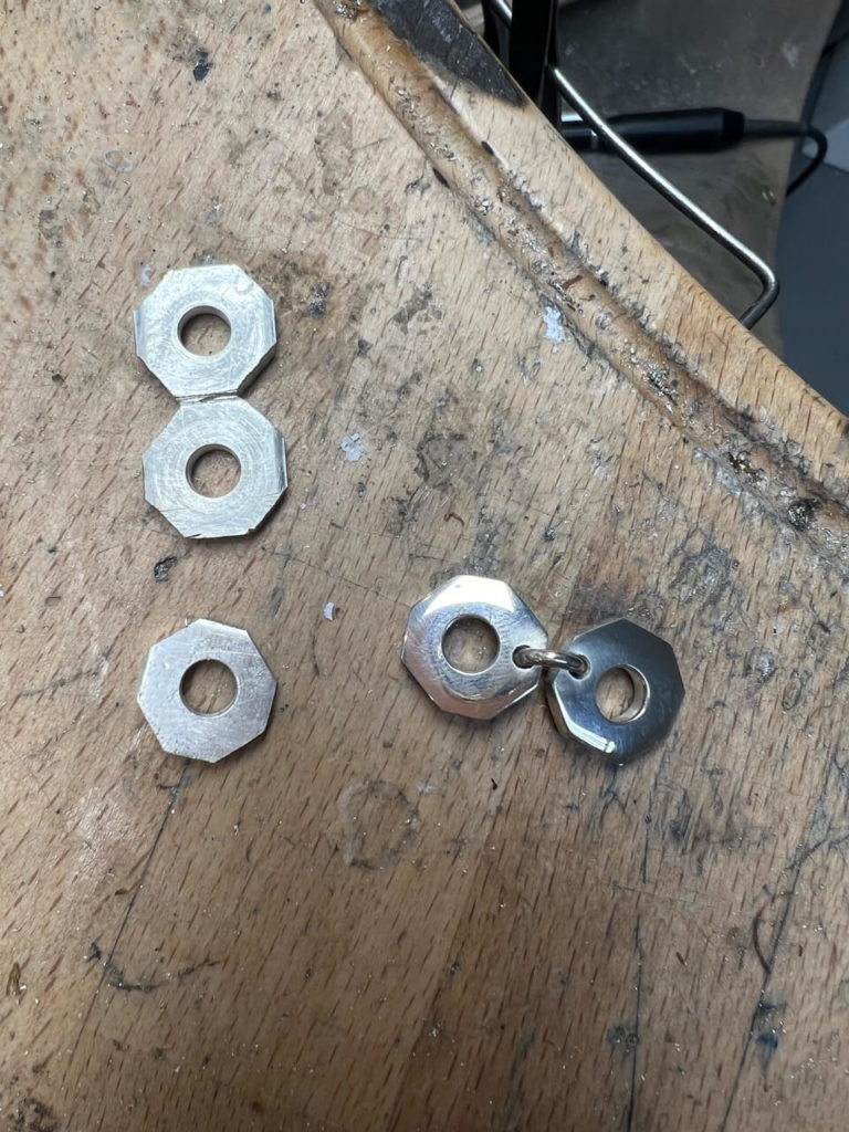 Handgefertigte Schmuckelemente in Sechskantform aus Silber auf einer hölzernen Werkbank in unserer Berliner Goldschmiede-Werkstatt.