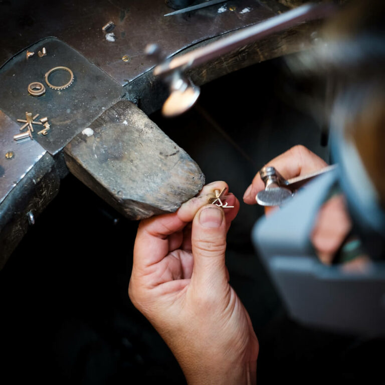 Goldschmiede Berlin-Lankwitz: Ein Juwelier, der an einer Werkbank sorgfältig ein Goldschmuckstück anfertigt und damit seine professionellen Reparatur- und Designleistungen präsentiert.