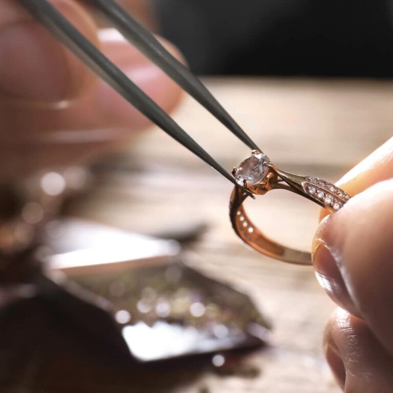 Ein Goldschmied prüft mit einer Pinzette einen filigranen Ring aus Roségold mit funkelndem Stein – professioneller Schmuck Service in Berlin-Lankwitz.